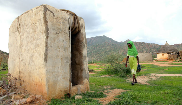 A girl walks towards the family toilet holding soap and water