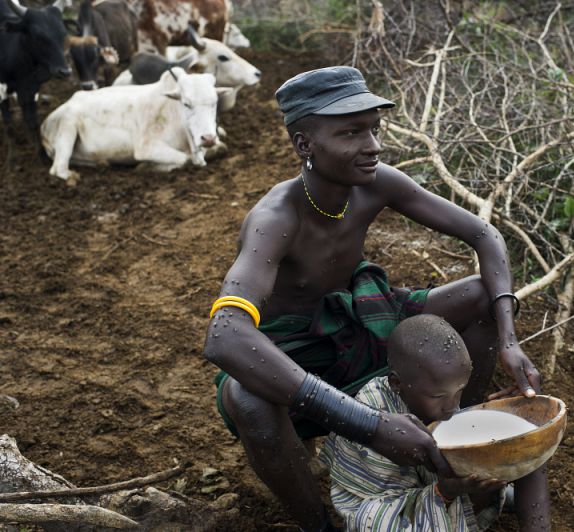 Karamojong pastoralist helps his son to drink milk