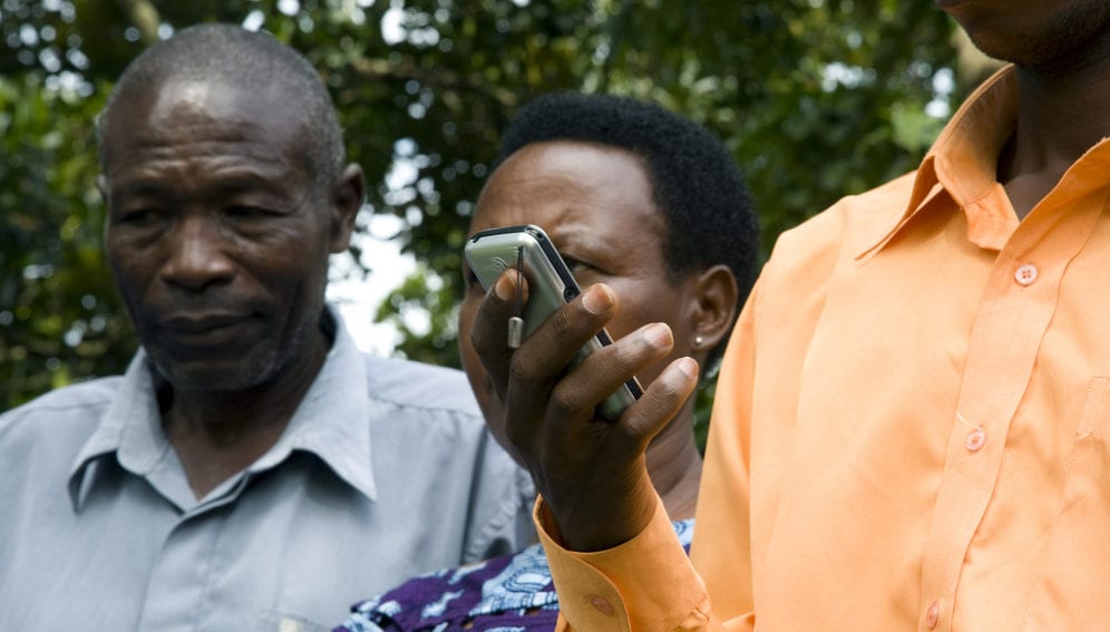 man_looks_at_mobile_phone_during_farmers_meeting_in_bwera_uganda jan.jpg