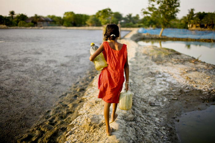 A girl carrying vessels home after collecting water from a pond