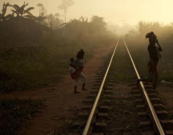 woman and a child carrying a baby cross the railway