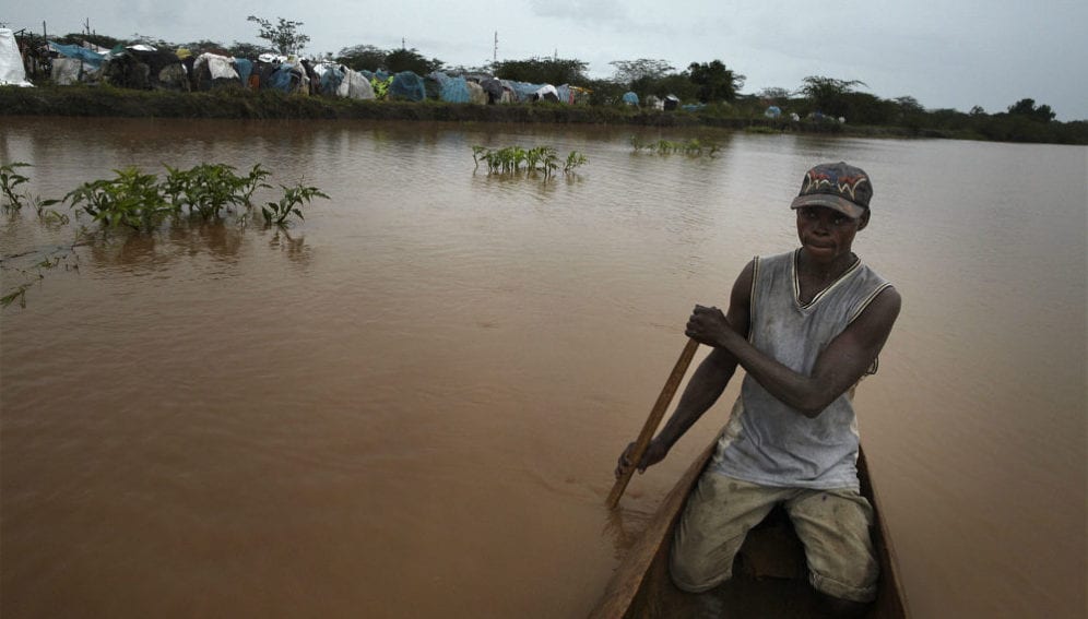 A man paddles past a camp for those displaced by the flooding of the Tana River