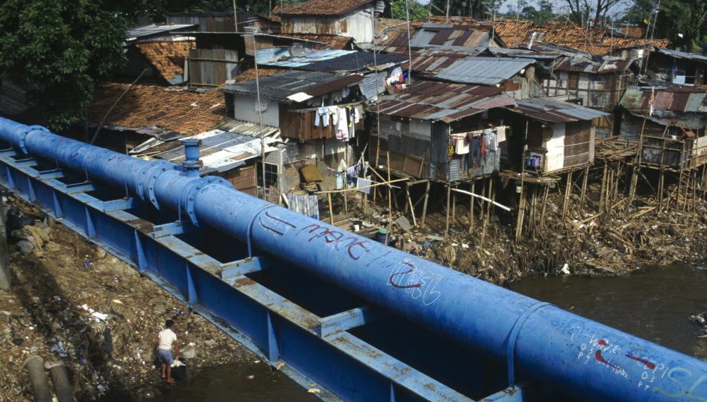 Slum housing by dirty waterway in the city, with a water pipe in the foreground
