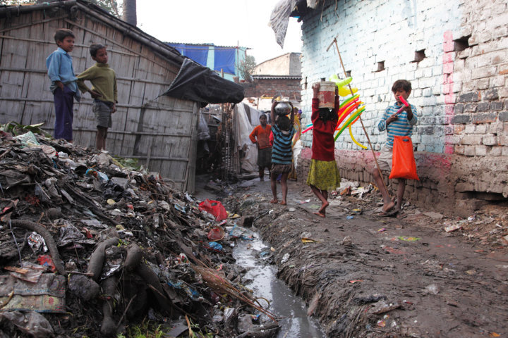 Kamla Nehru Nagar slum, Bihar. This state in north-east India is one of the least economically and socially developed in the country. Here, children carry water past an open sewer and a mound of rubbish. In India, 186,000 children die every year from diarrhoea largely caused by unsafe water and sanitation
