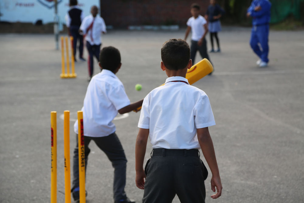 Children play cricket in the playground. Kids can attend after-school clubs and holiday programmes, which get them off the street and learning sport, the deputy principal tells me
