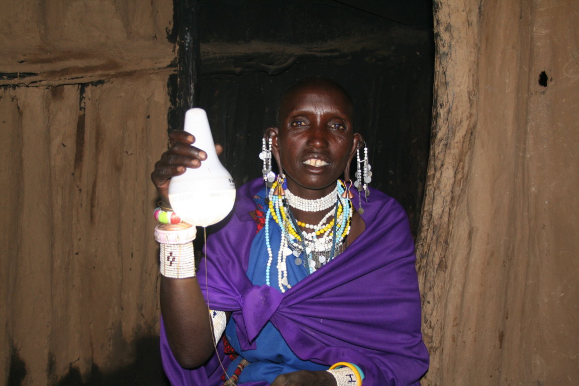 Nailah holds up her solar-charged light. Her children can read their school books indoors and she can make money by taking payment from neighbours in return for charging their mobile phones.
