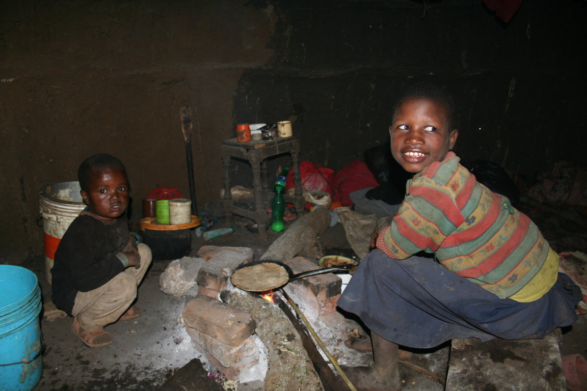 The dark, smoky interior of a traditional Maasai hut. Children sit around the traditional cooking arrangement based on three stones. Smoke stings the eyes and catches the back of the throat.
