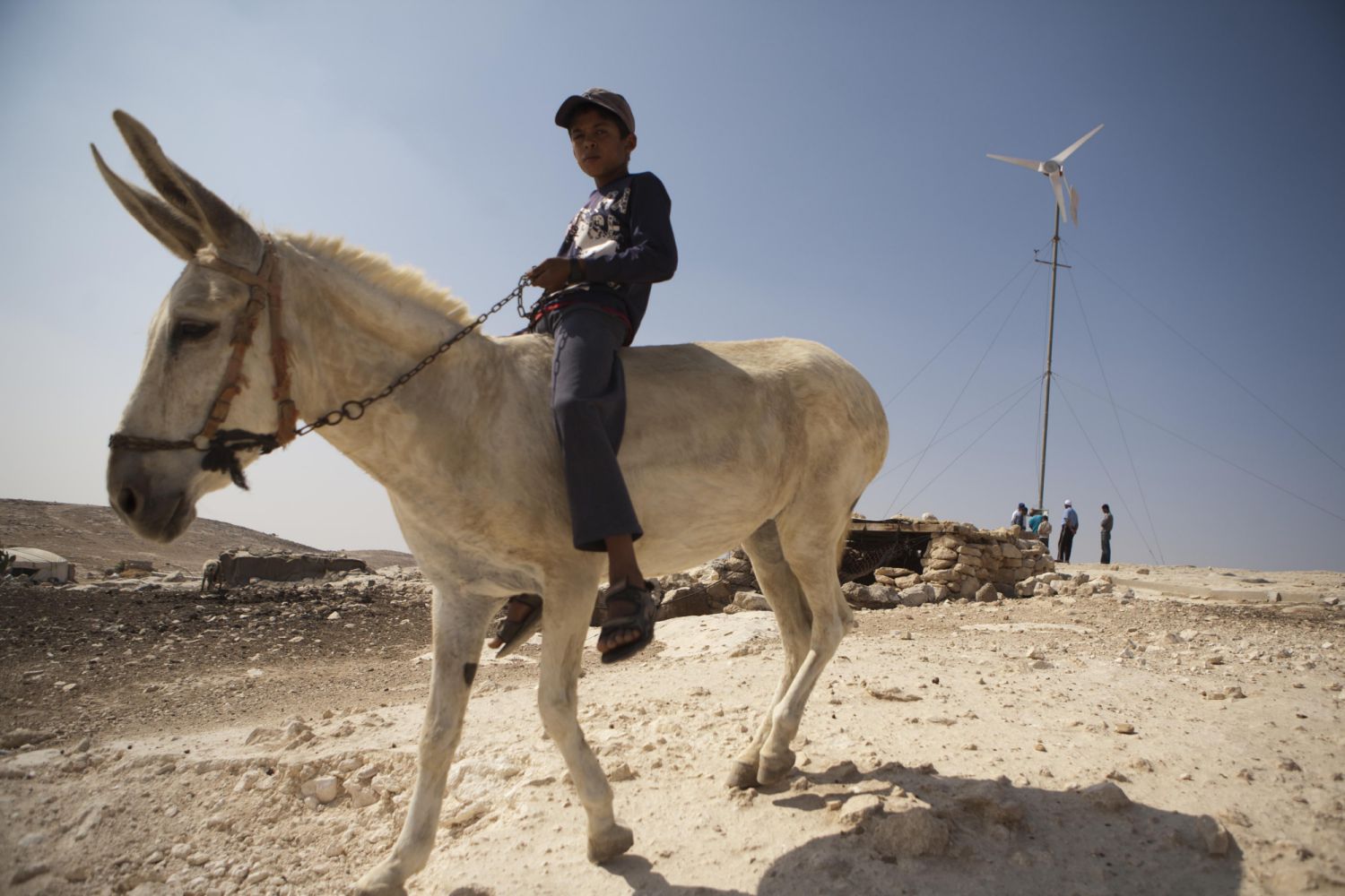 A young boy on a donkey near a wind turbine in Tuba village, Mount Hebron. The main livelihood in the region comes from animals such as goats and sheep
