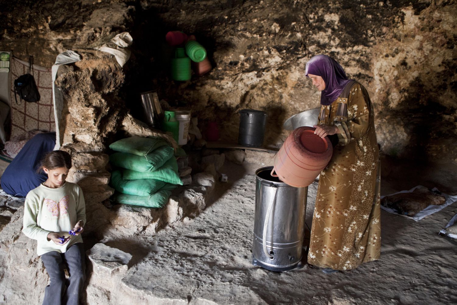 A woman pours milk into a new butter churner, powered by renewable energy. Electric churners slash the time it takes women to make butter and cheese &mdash; one of the staple livelihoods here. Many of the villagers in the Mount Hebron hills live in caves such as this one in Tuba&nbsp;
