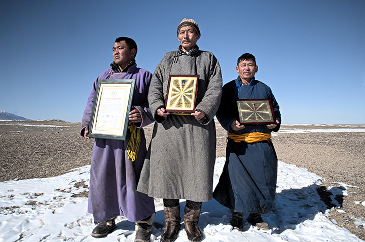 
	Batkhuyag Tseveravajaa, head of the Uvurkhangai community in the Gobi desert, with two herders from the same community display the national and provincial awards they received as an acknowledgement for having taken the initiative to improve pasture managementto solve environmental challenges.
