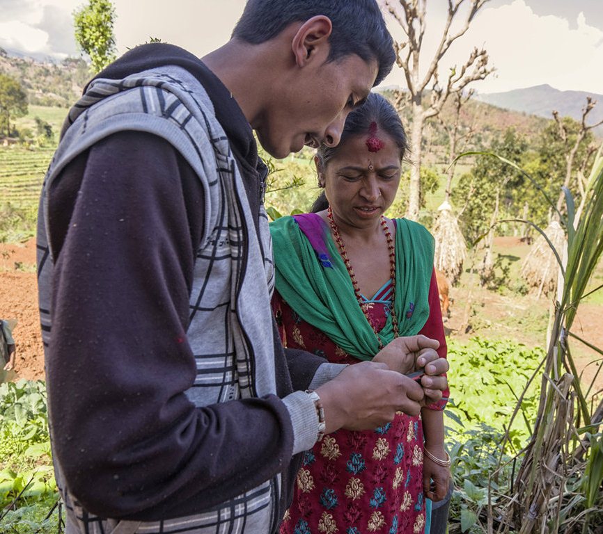 A woman and her son check crop prices on a mobile phone via text message. The message contains wholesale market prices from the Nepal Agricultural Research Council, helping farmers decide on the best day to sell their produce to maximise profit
