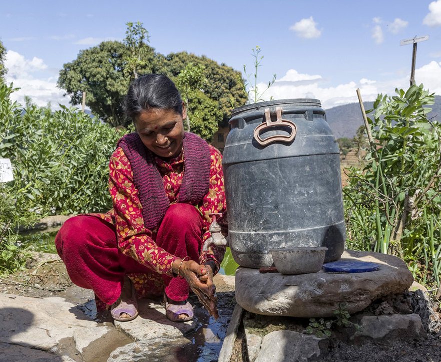 A woman washes her hands in recycled kitchen water after working in her field. A pipe connects the drainage pipe of the sink to a container, so water can be used again for tasks such as cleaning
