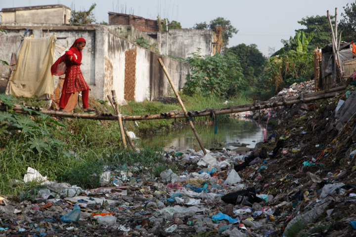 A girl crosses a makeshift bridge above an open sewer in the Kamla Nehru Nagar slum, India. The sewer is also used as a toilet and a rubbish dump. Young children have fallen off this bamboo bridge and drowned. Two-thirds of Indians, or 791 million people, lack access to adequate sanitation, according to WaterAid
